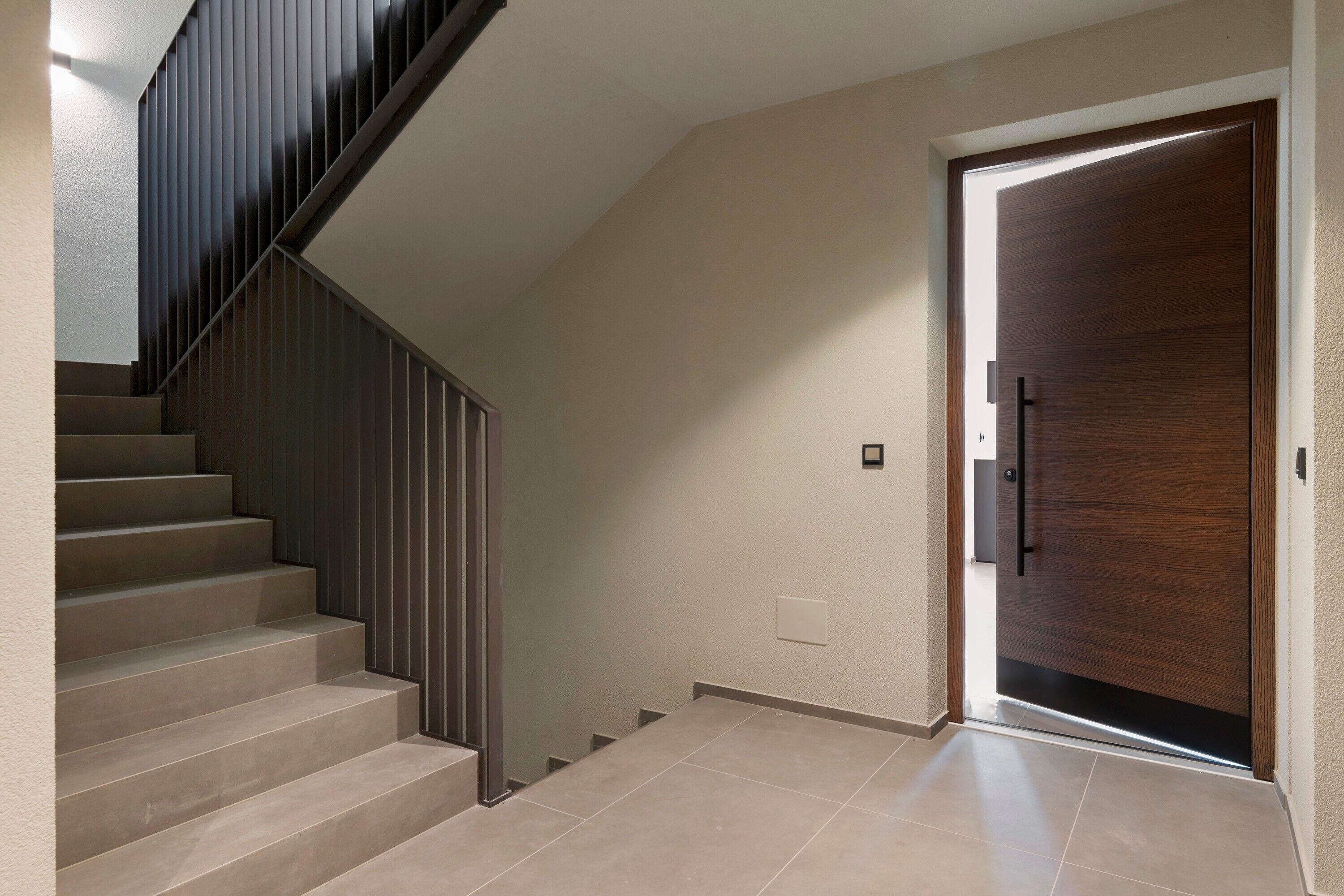 A staircase with a modern design, a wooden door, and a light switch on the wall.