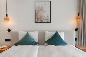 A hotel room with a bed, two pillows, a nightstand, a framed picture on the wall, and two wall-mounted lamps.