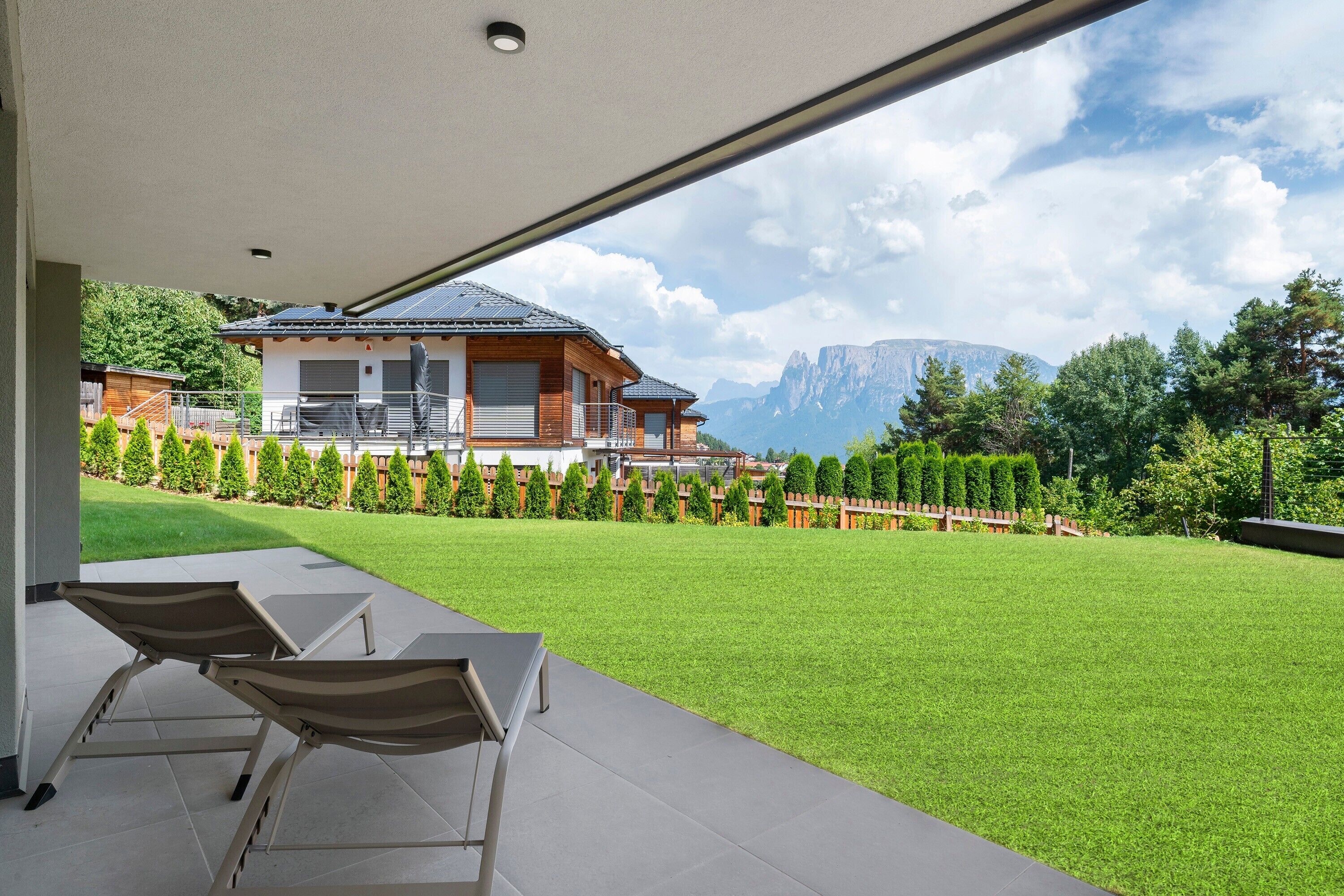 A modern house with a covered patio, a well-maintained lawn, and a mountain view.