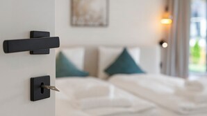 Habitación de hotel con cama, una puerta con mirilla y ventana con vista a follaje.