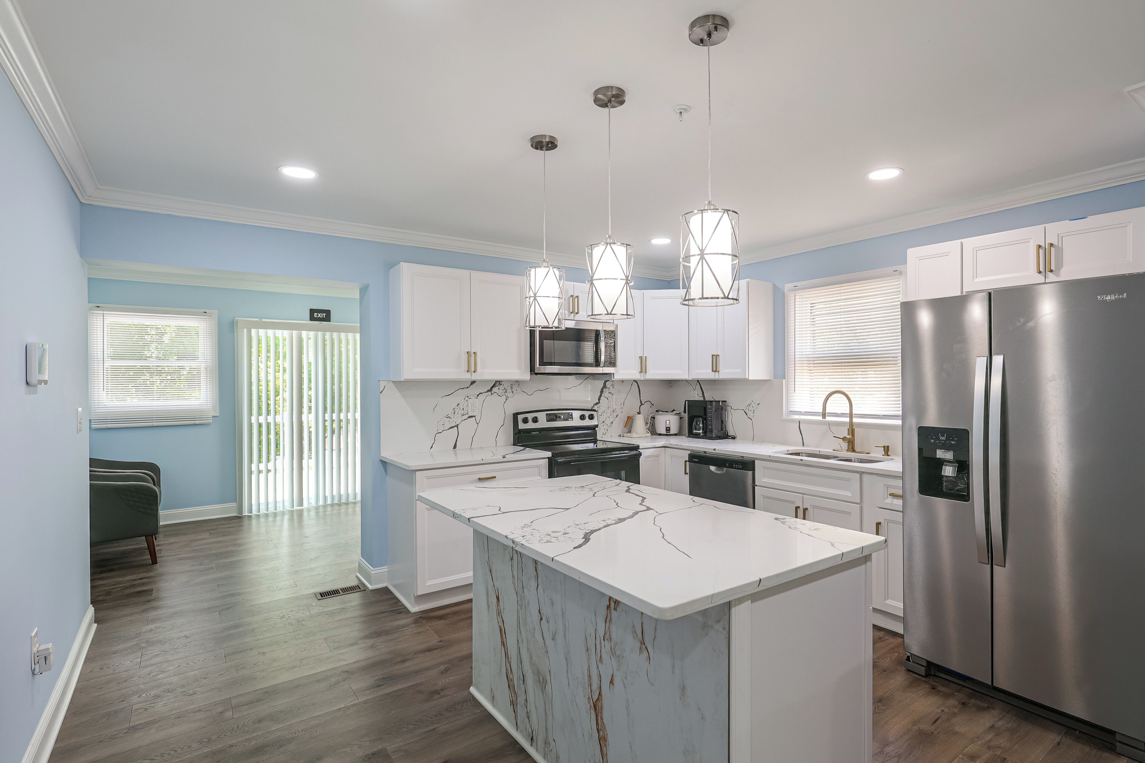 A modern kitchen with white cabinetry, a stainless steel refrigerator, and pendant lights.