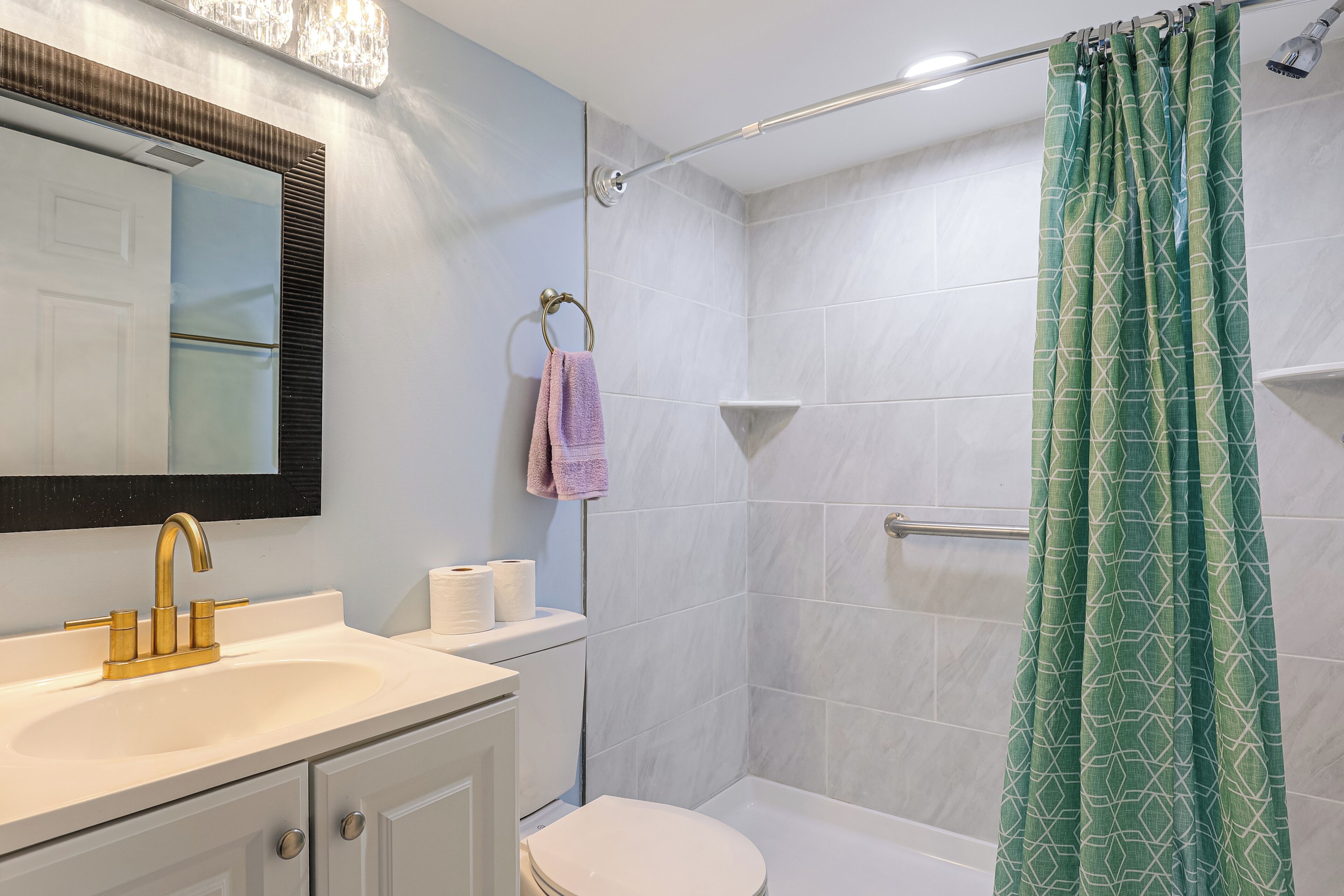 Een badkamer met een witte wasbak, een spiegel, een toilet en een douche met een groen patroon gordijn.