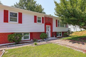 A two-story house with a red and white exterior, a front porch, and a small front yard with a lawn and a flower bed. - Family Home w/ Fenced Backyard, 16 Mi to DC! (Clinton)