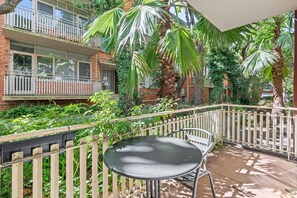 Ein Balkon mit Tisch und Stühlen, umgeben von einem Holzzaun und üppiger Bepflanzung.