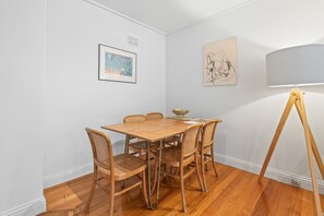 A dining area with a wooden table and wicker chairs, a floor lamp, and two framed artworks on the walls. - Charming Inner-City Stay- Space, Style & Location (Toorak)