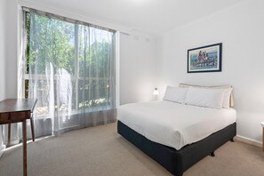 Ein Schlafzimmer mit Bett, Schreibtisch und einem Fenster mit durchsichtigen Vorhängen.