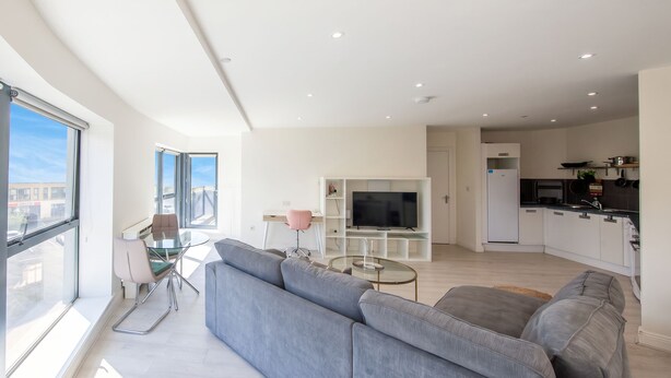 A modern living room with a grey sofa, a glass coffee table, and a TV.