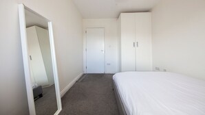 A bedroom with a single bed, a wardrobe, a mirror, and a door.