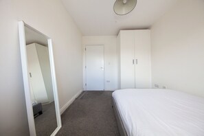 A bedroom with a single bed, a wardrobe, a mirror, and a door.