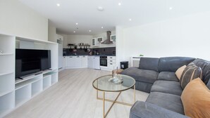 A modern living room with a grey sofa, a glass coffee table, and a TV on a white stand.