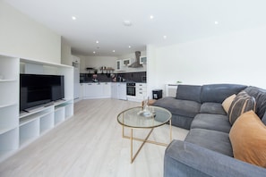 A modern living room with a grey sofa, a glass coffee table, and a TV on a white stand.