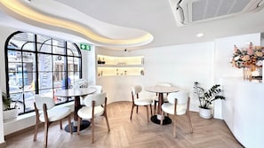 A modern interior with a round table and chairs, a large window with a view of the street, and a wall-mounted shelf with decorative items. - VINA VILLE hotel Bangkok (Bangkok)