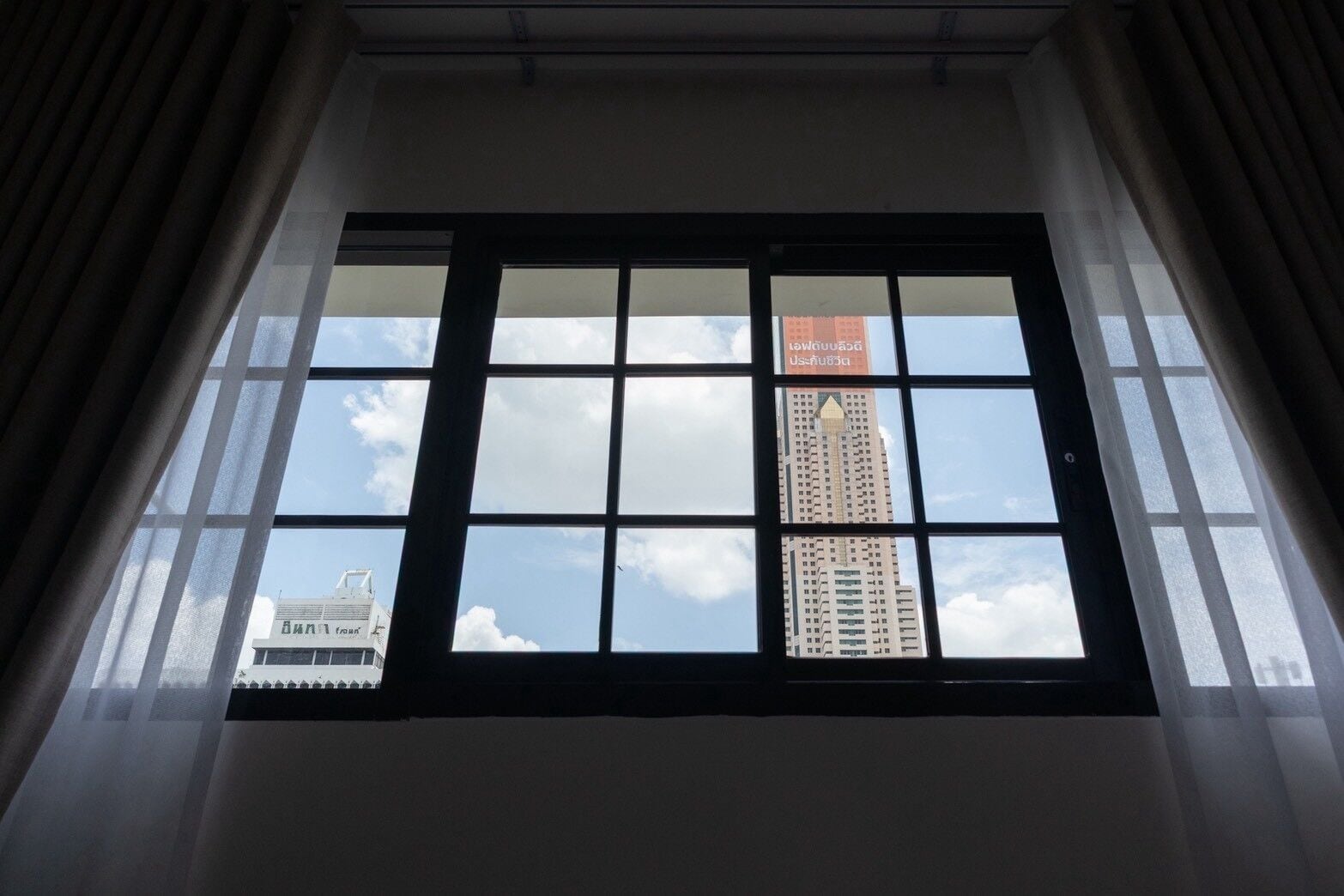Uma janela com vista para um edifício alto e uma construção menor ao fundo.