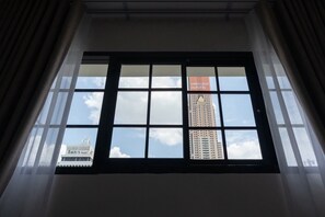 Uma janela com vista para um edifício alto e uma construção menor ao fundo.