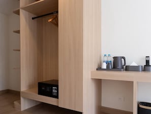A modern room with a built-in microwave, a wooden wardrobe, and a small shelf with a kettle, bottles, and a remote control. - VINA VILLE hotel Bangkok (Bangkok)