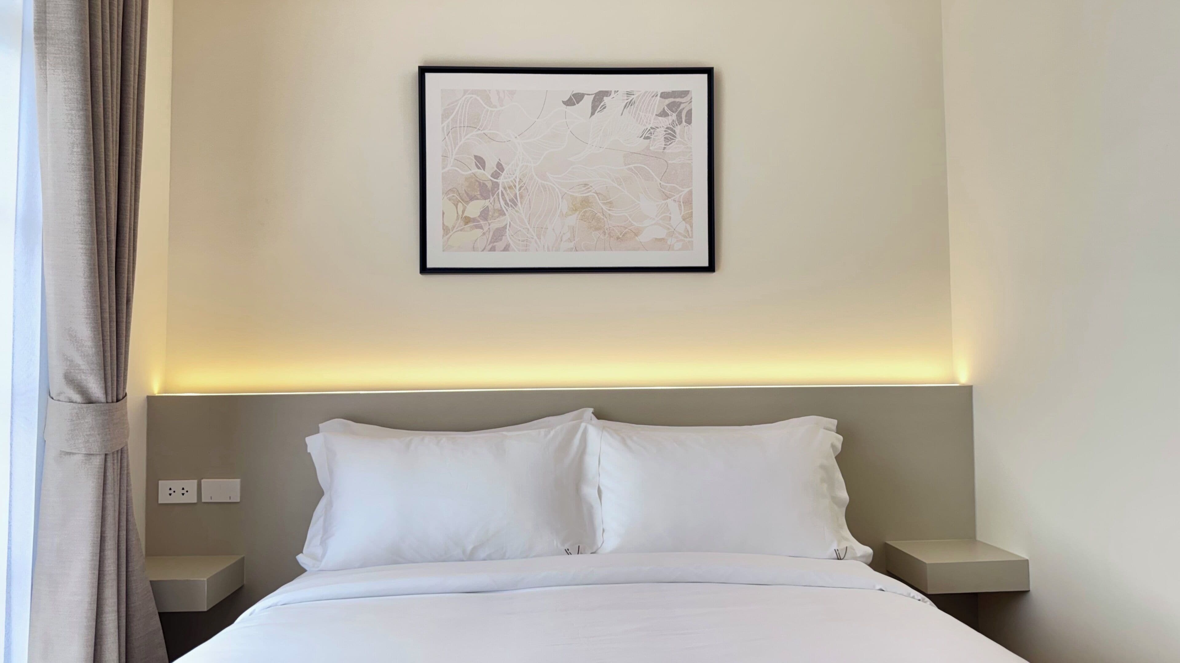 A hotel room with a bed, two bedside tables, a wall-mounted light, and a framed abstract artwork.