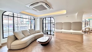 Un interior moderno con un sofá curvo, una mesa de centro de madera y amplias ventanas con vistas a la calle.