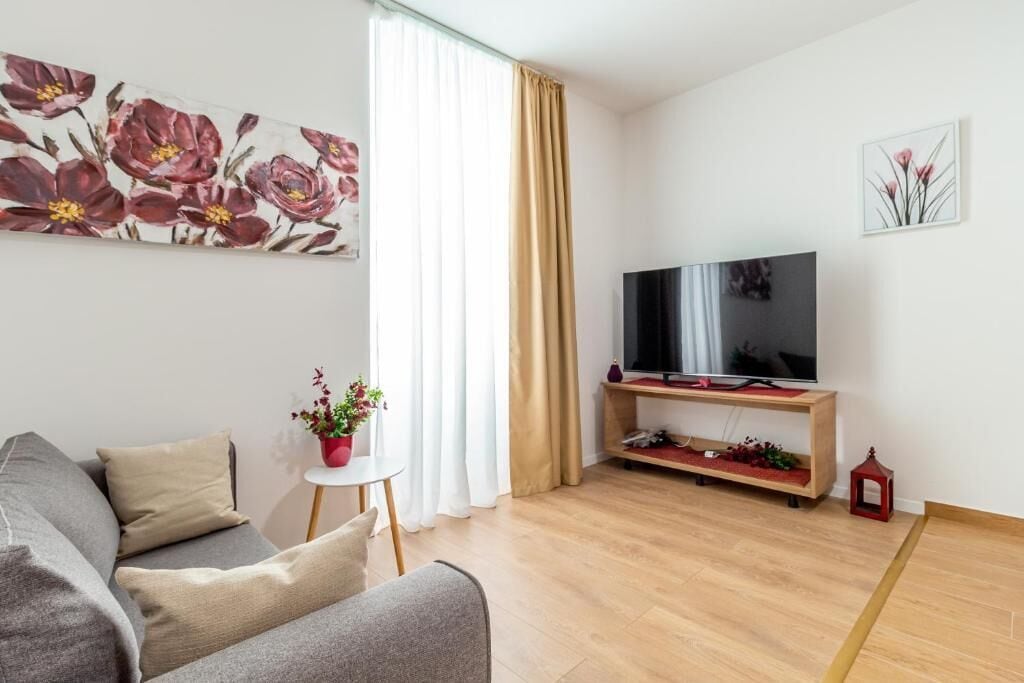 Una sala moderna con un sofá, un televisor sobre un mueble bajo, una mesita con una planta y un farolillo rojo.