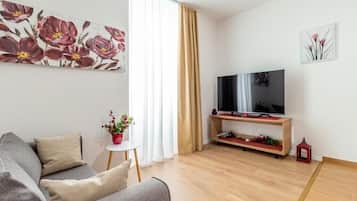 Una sala moderna con un sofá, un televisor sobre un mueble bajo, una mesita con una planta y un farolillo rojo.
