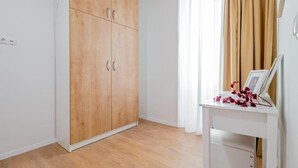 A room with a wooden wardrobe, a white desk with a picture frame, and a window with curtains.