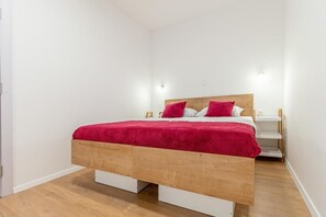 Habitación con una cama individual, cabecera de madera, ropa de cama blanca y una manta roja.