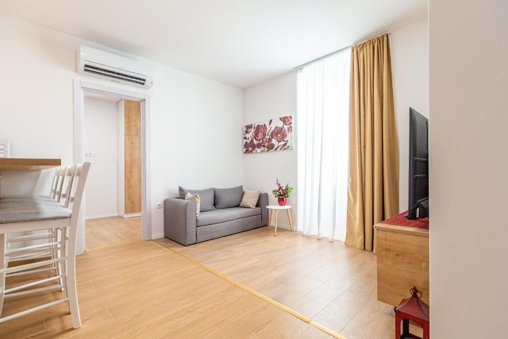 A living room with a sofa, a small table with a plant, a TV, and a wooden floor.