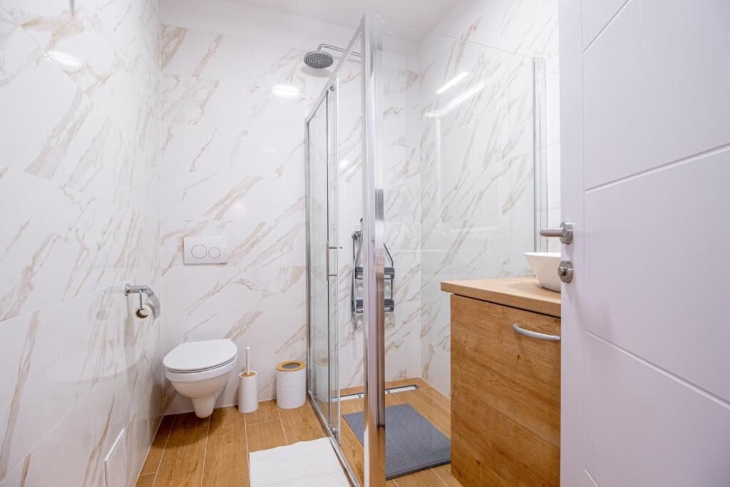 Un baño moderno con cabina de ducha de vidrio, inodoro y tocador de madera.
