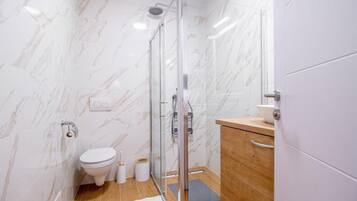 Un baño moderno con cabina de ducha de vidrio, inodoro y tocador de madera.