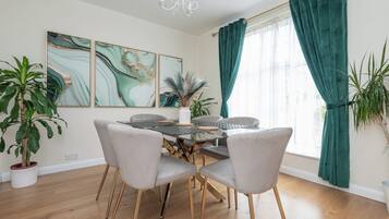 A dining area with a glass-top table, four chairs, and a vase with a plant.