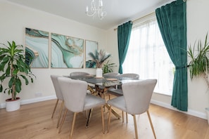A dining area with a glass-top table, four chairs, and a vase with a plant. - Inviting 3BDR Garden Home in Sanderstead (Greater London)