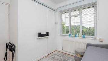 A bedroom with a white wardrobe, a radiator, a window with blinds, and a grey sofa.