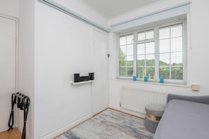 A bedroom with a white wardrobe, a radiator, a window with blinds, and a grey sofa. - Inviting 3BDR Garden Home in Sanderstead (Greater London)