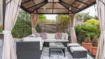An outdoor patio with a covered seating area, including a sofa and two side tables.