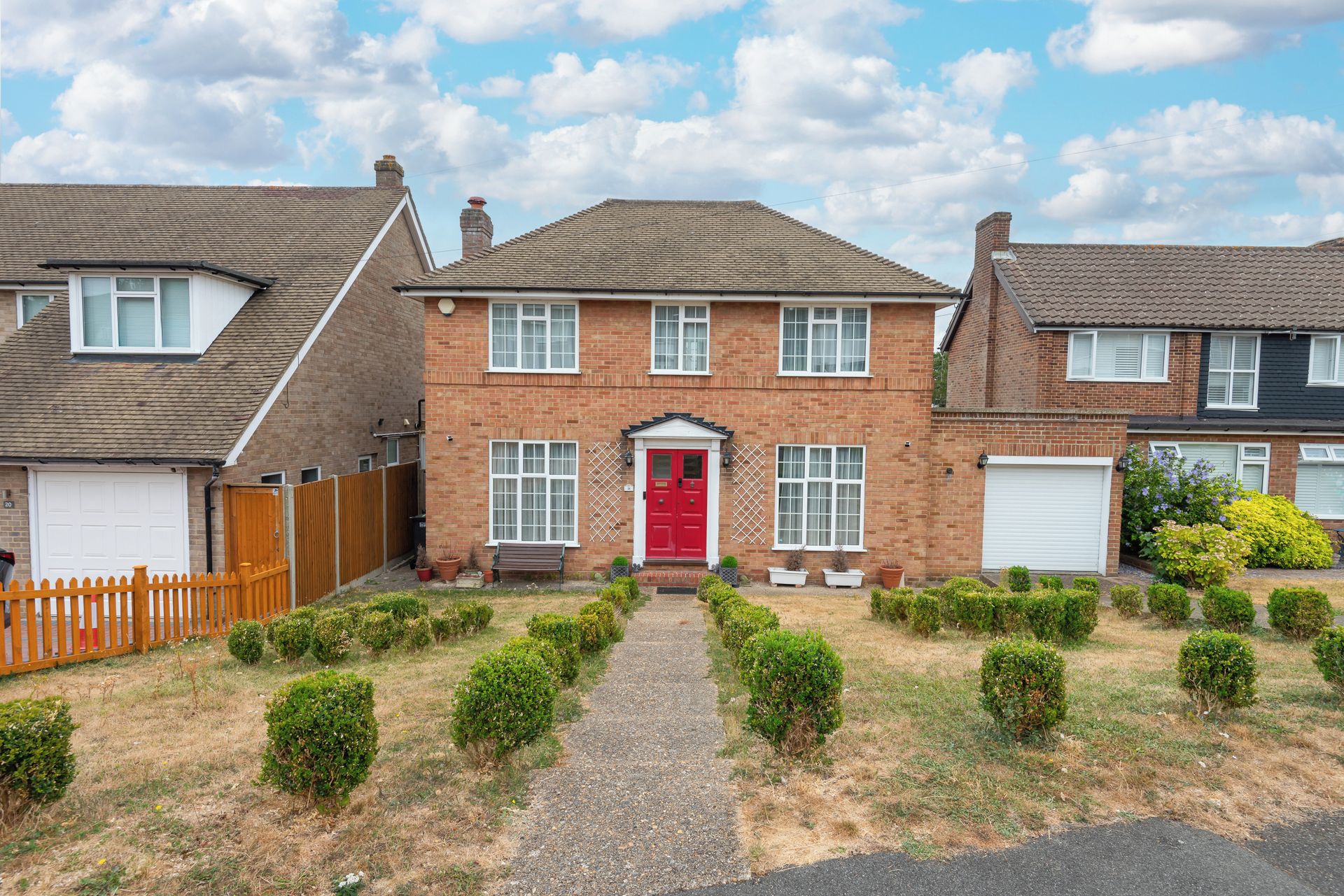 A two-story brick house with a red front door, a driveway, and a wooden fence.