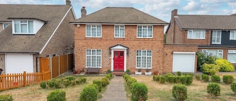 A two-story brick house with a red front door, a driveway, and a wooden fence.