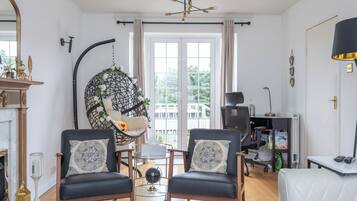 A living room with two black leather chairs, a glass coffee table, a hanging chair with white flowers, a fireplace, and a view of the outdoors through a large window.