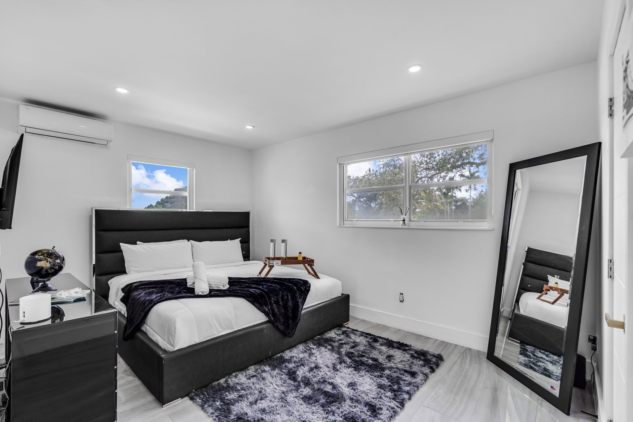 A modern bedroom with a large bed, a bedside table, a globe, and a window with a view of trees.