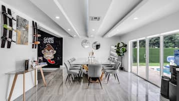 Een moderne eetruimte met een glazen tafel, grijs beklede stoelen en een grote poster aan de muur.