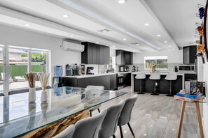 A modern kitchen with a glass dining table, black cabinets, and a view of the outdoors. - Miami Resort Villa with Jacuzzi & Sauna (Miami)