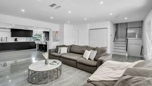 Ein modernes Wohnzimmer mit einer Couch, einem Couchtisch und einer Küche im Hintergrund.