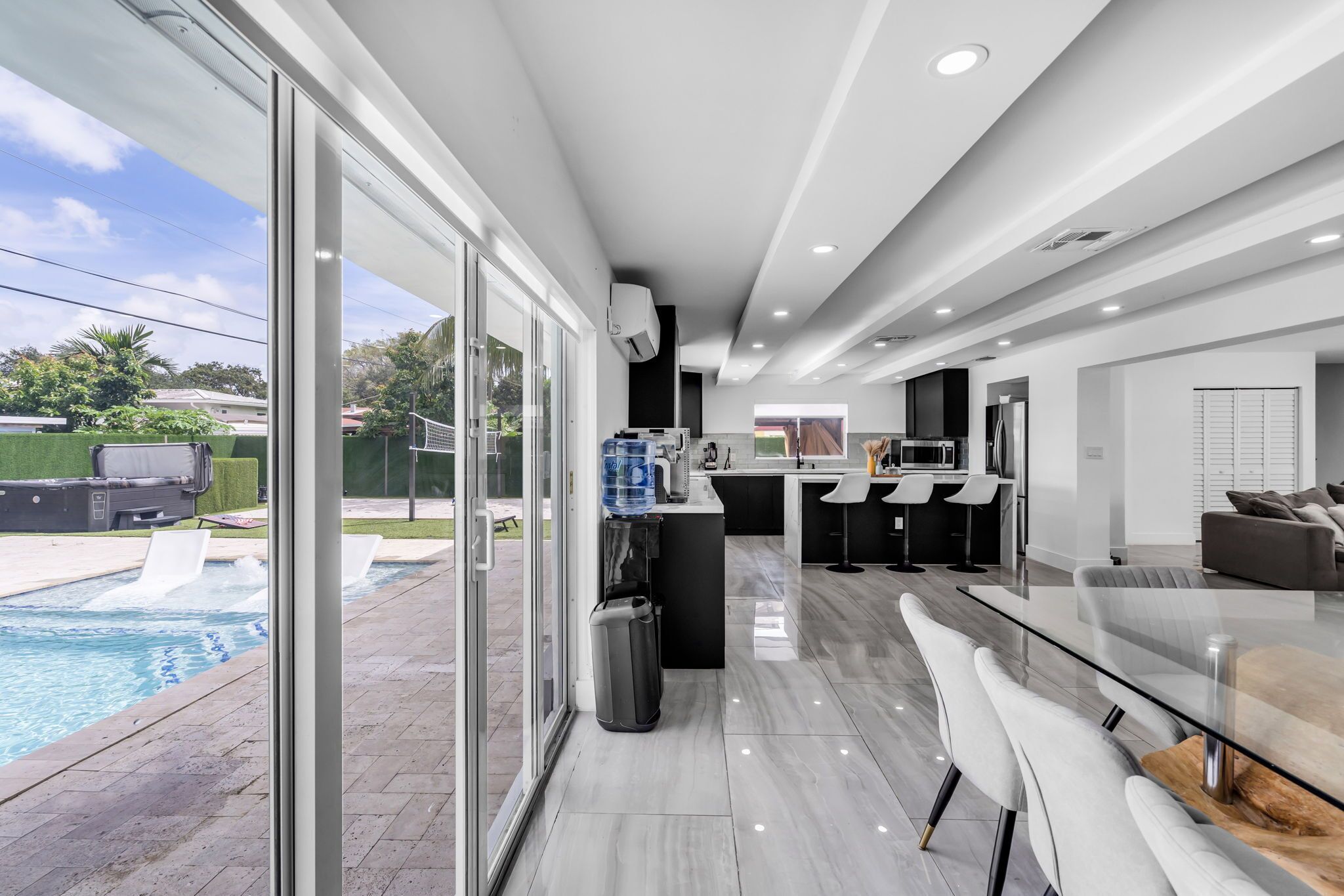 A modern kitchen with a large island, a dining area with bar stools, and a view of a swimming pool.