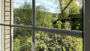 A view through a window with a stone wall and a lush green landscape with trees and shrubs. - Spacious, detached villa for 12 people near Winterberg (Grönebach)
