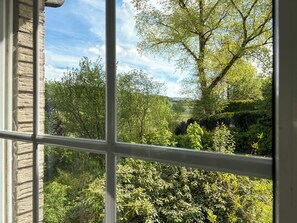 Blick durch ein Fenster auf eine steine Mauer und eine üppige grüne Landschaft mit Bäumen und Sträuchern.
