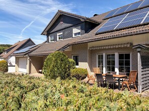 Ein Wohnhaus mit Solaranlage, einer Terrasse mit Gartenmöbeln und einem gepflegten Garten.
