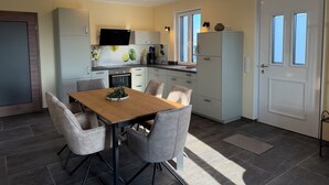 A modern kitchen with a dining area, featuring cabinets, a TV, and a refrigerator. - Newly Built Farmhouse-Style Vacation Rental Near the Borders of Luxembourg and Belgium (Üttfeld)