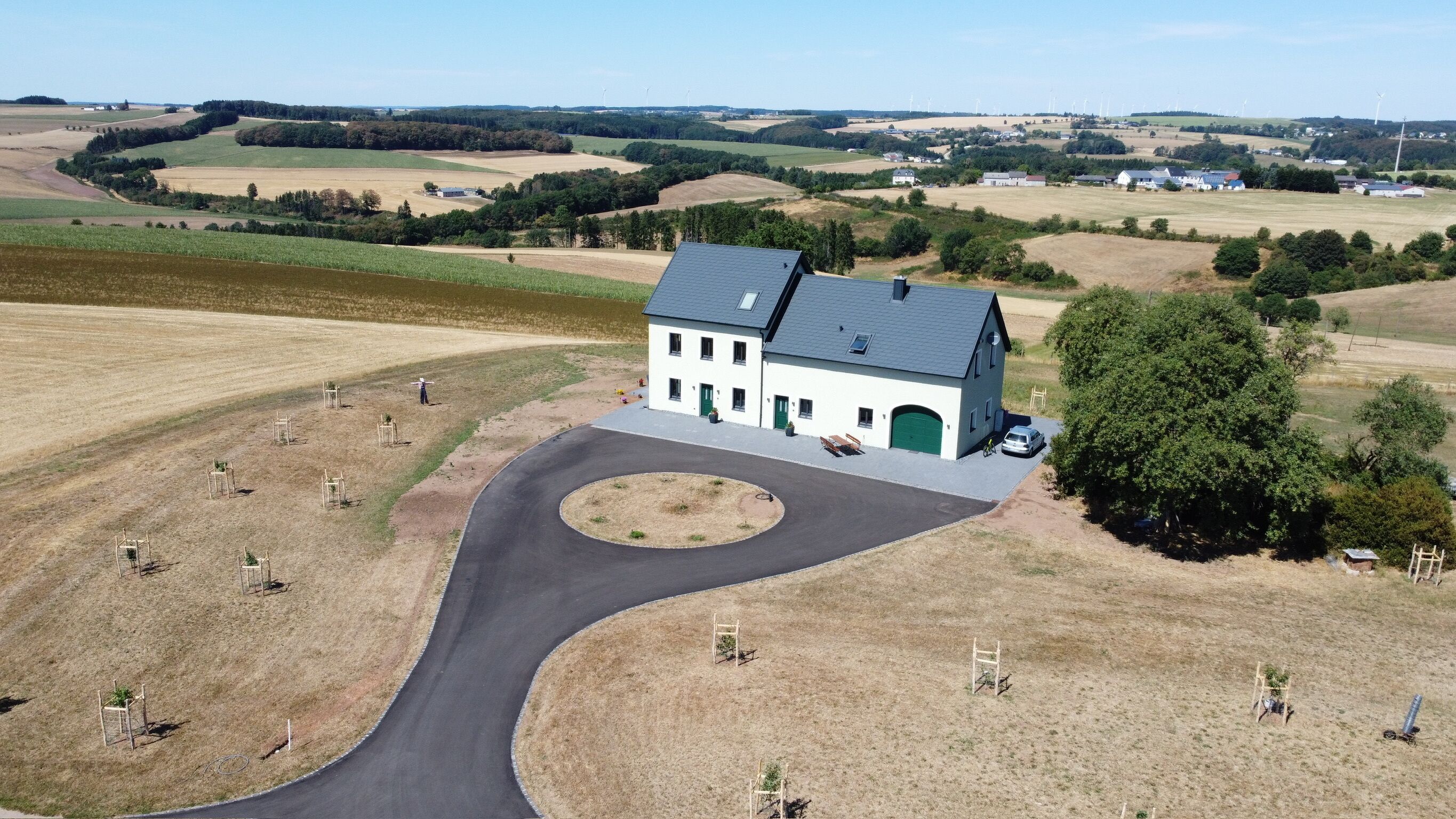 Un bâtiment blanc avec un toit gris, une allée et une voie d’accès circulaire.
