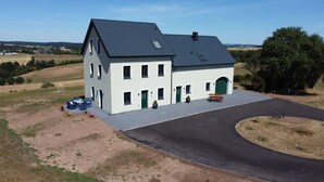A two-story house with a paved driveway and a bench. - Newly Built Farmhouse-Style Vacation Rental Near the Borders of Luxembourg and Belgium (Üttfeld)