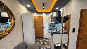 A hallway with a sofa, a mirror, a door, and a kitchen area with patterned tiles.