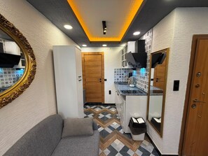 A hallway with a sofa, a mirror, a door, and a kitchen area with patterned tiles.