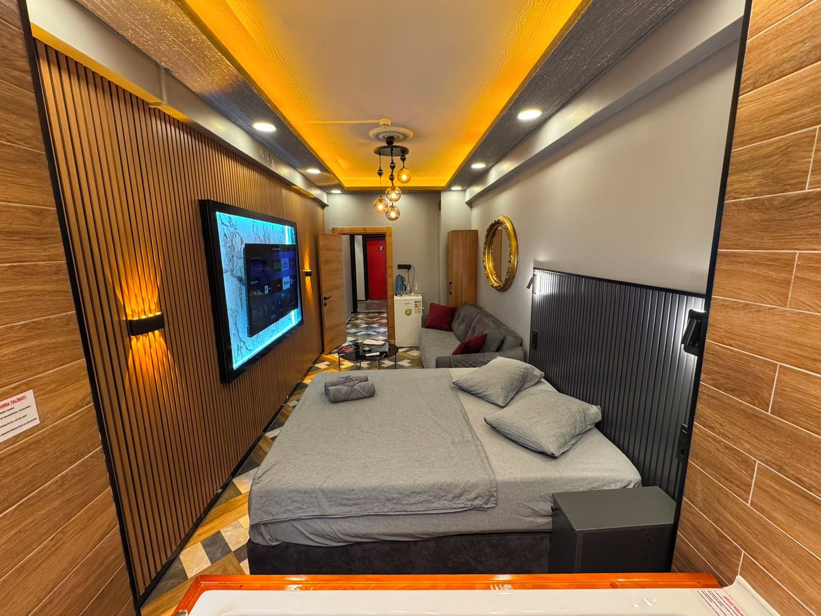 Habitación de hotel moderna con una cama, un televisor montado en la pared, un diseño de paneles de madera y un espejo.